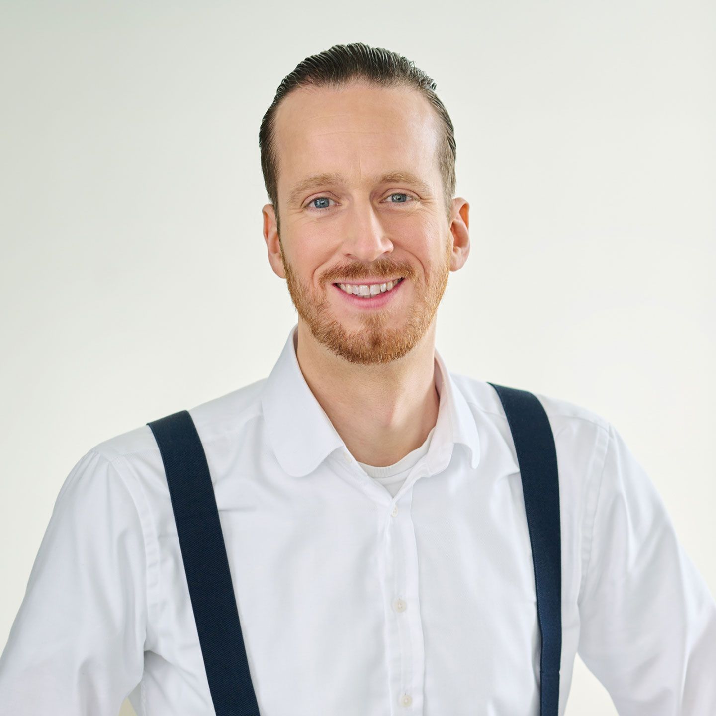 Sebastian Pollmer, egy fehér inget és kék nadrágtartót viselő férfi áll egy világos szobában. 