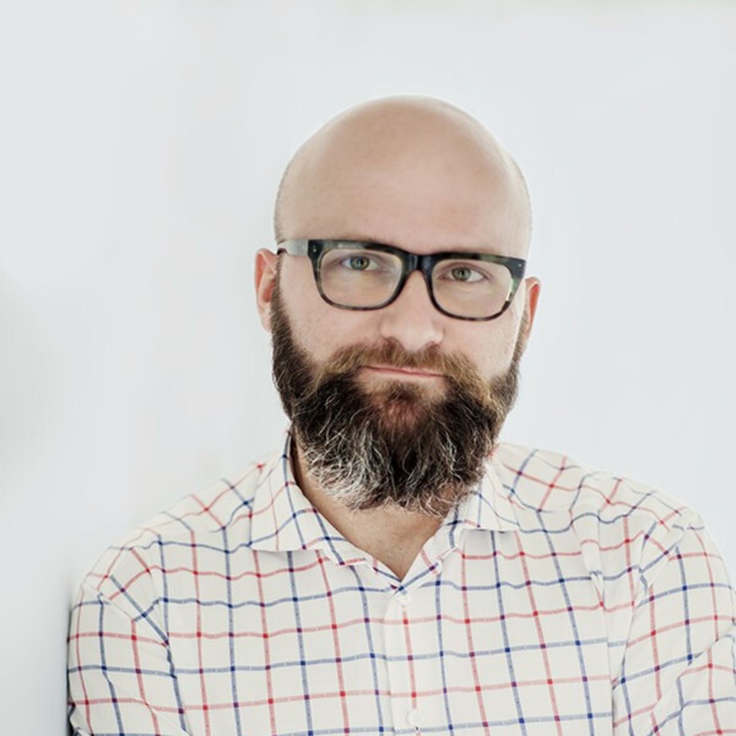 Dr. hab. Tomasz Piekot kockás ingben támaszkodik egy fehér falnak.
