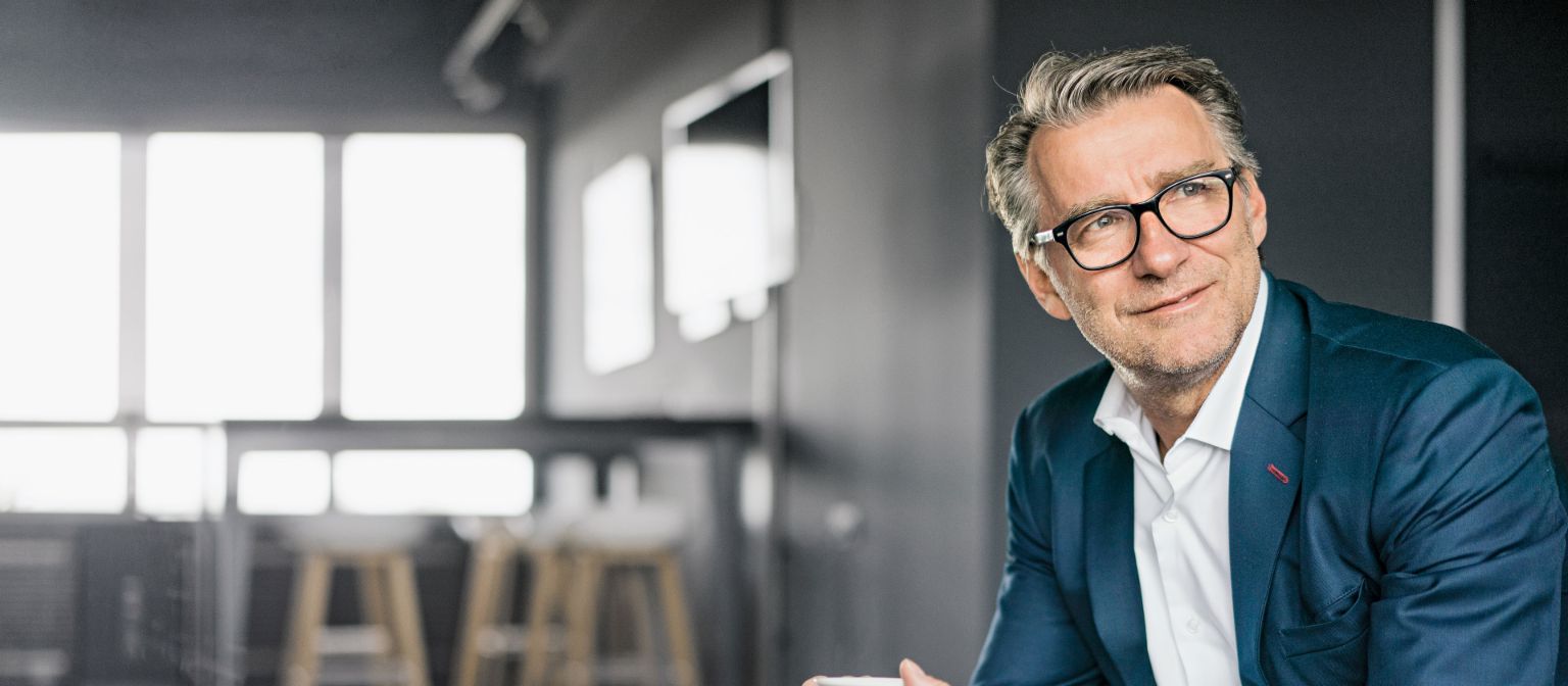 Egy ülő, érett üzletember portréja, aki kék öltönyt visel és fehér kávéscsészét tart