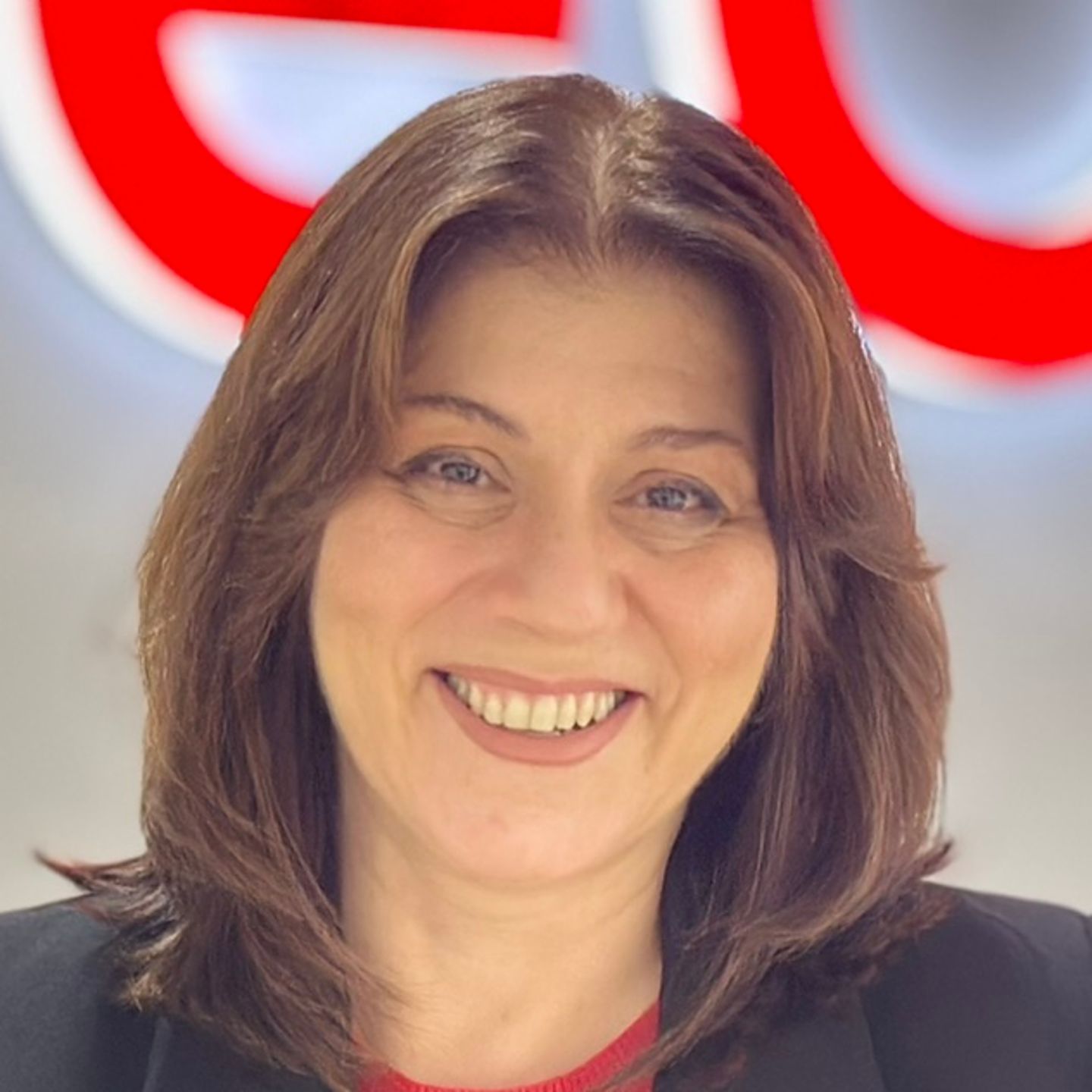 Belén Barreiro, a spanyolországi EOS Contact Center ügynöke egy fekete blézerben támaszkodik a pultnak egy fényes EOS logó előtt.