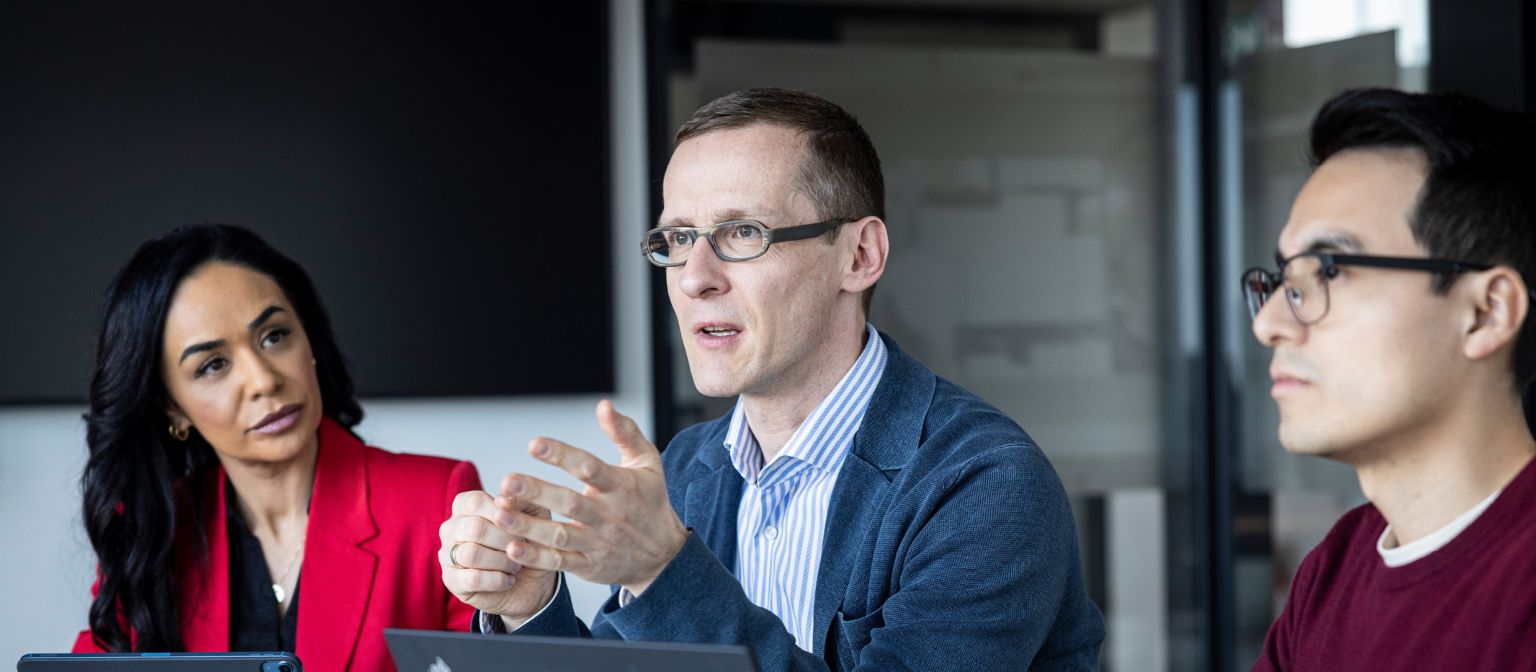 Három személy beszélget egy irodában.