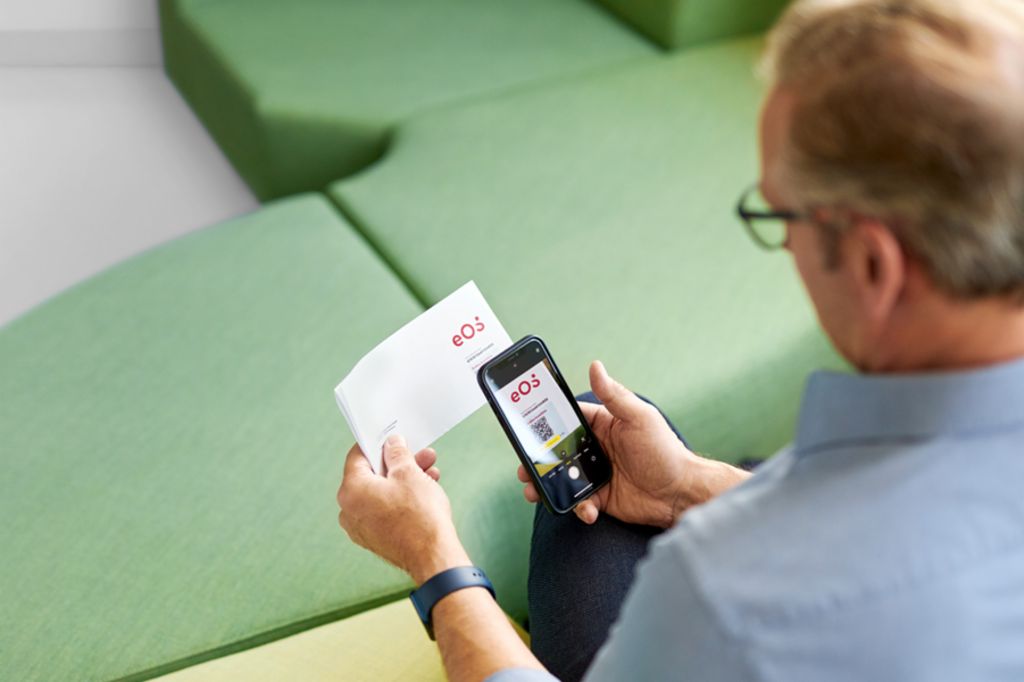 Egy férfi QR-kódot olvas be az EOS-tól kapott levélen a smartphone-jával, hogy online rendezze nyitott követelését az EOS Portálon.