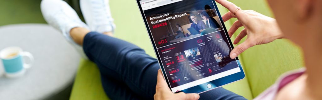 Személy zöld kanapén, aki az EOS 2024/25-ös Éves és Fenntarthatósági Jelentését nézi egy táblagépen