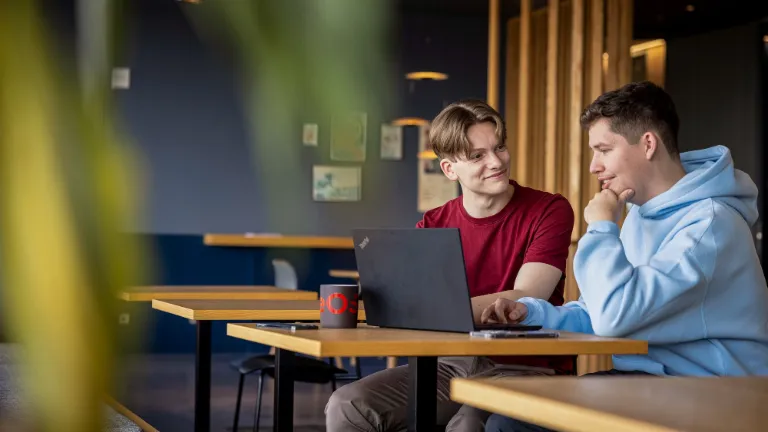 Két munkatárs laptopon dolgozik együtt, elősegítve a partnerséget és a méltányosságot a munkahelyen.