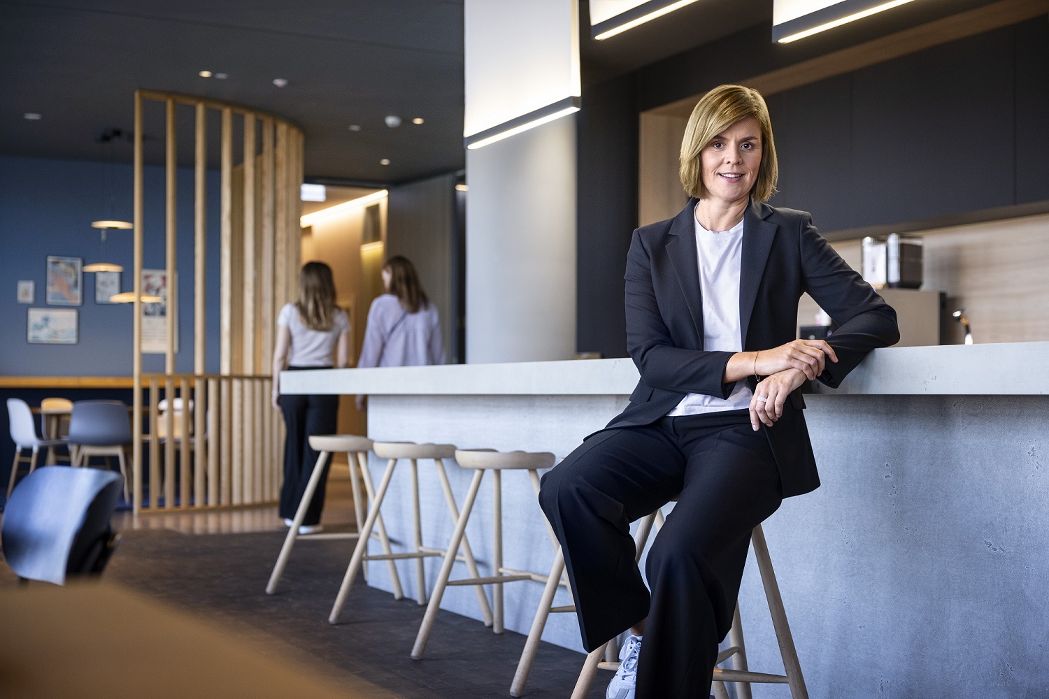 Dr. Eva Griewel, az EOS Csoport pénzügyi igazgatója (CFO), egy társadalmi térben ül egy magas széken, fekete zakót viselve.